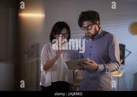Two business partners standing and using digital tablet in their teamwork they working till late at office Stock Photo