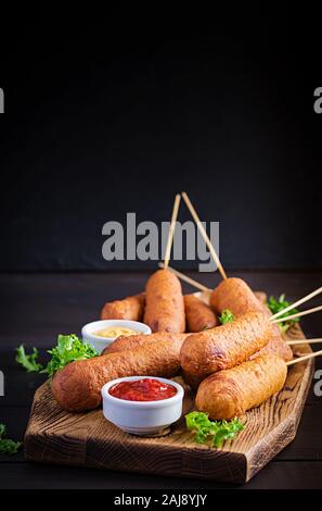 Traditional American corn dogs with mustard and ketchup on wooden board. Street food. Copy space Stock Photo