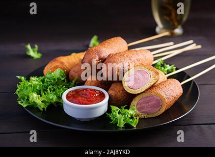 Traditional American corn dogs with mustard and ketchup on black plate. Street food. Copy space Stock Photo