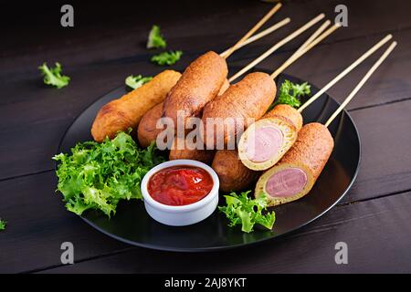 Traditional American corn dogs with mustard and ketchup on black plate. Street food. Copy space Stock Photo