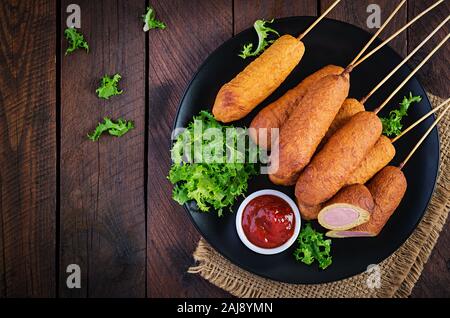 Traditional American corn dogs with mustard and ketchup on black plate. Street food. Top view, copy space Stock Photo