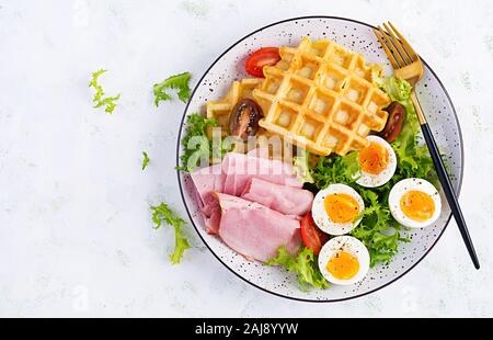 Breakfast with cornmeal waffles, boiled egg, ham and tomato on white background. Appetizers, snack, brunch. Healthy food. Top view, overhead, copy spa Stock Photo