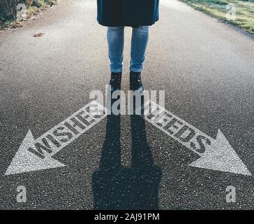 person standing behind arrows on asphalt pointing in different directions saying WISHES and NEEDS Stock Photo