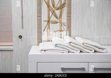 Close-up of white folded towels on the white dresser in modern bathroom. Stock Photo