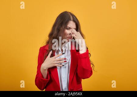 Unhappy woman in white shirt and red jacket covers nose from bad smell Stock Photo