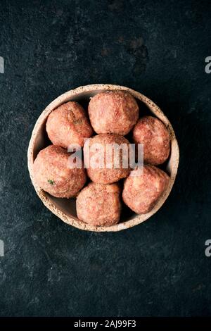 high angle view some raw homemade meatballs in a rustic earthenware plate, on a black stone table or countertop Stock Photo