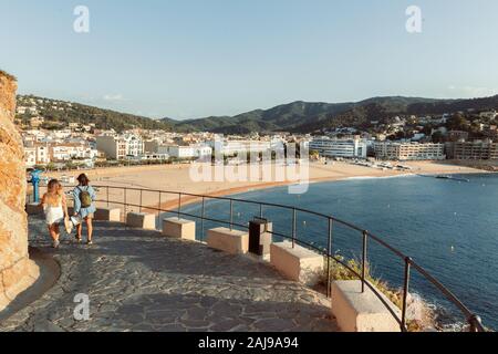TOSSA DE MAR,SPAIN - AUGUST 2, 2019: Two unknown girls go down to the sea from an ancient fortress on the seashore in the early morning. Stock Photo