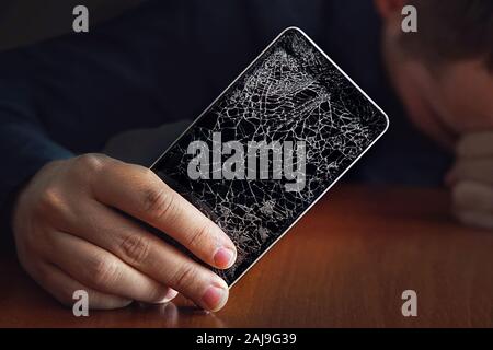 Handsome angry businessman showing broken smartphone with crashed screen. a large crack in the form of a web on the smartphone screen close-up. Stock Photo