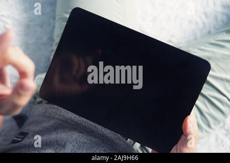 Close up of a young man raising the left index finger over the black screen of a digital tablet. Person starts working on tablet at home. Lying man ho Stock Photo