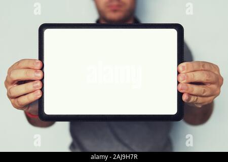 Close up of a digital tablet in man's hands at the blurred background. Lower half shot of a man's face. Holding a tablet with white screen in hands. P Stock Photo