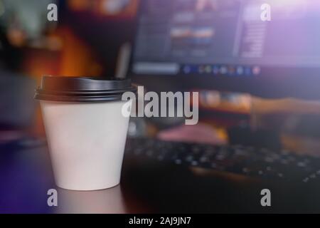 A cup of coffee takeaway on the desk with a monitor on background Stock Photo