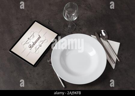 Tablet with stylish restaurant logo and laid table Stock Photo