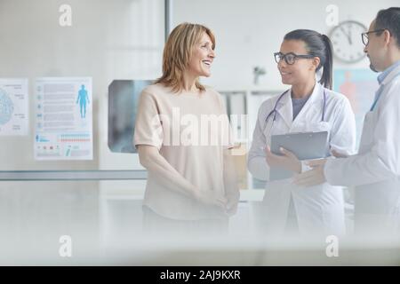 Happy mature woman smiling and talking to male doctor and nurse at the medical clinic Stock Photo