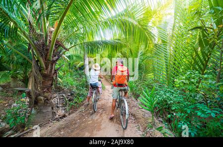 Tourist couple riding bicycle in the Mekong Delta region, Ben Tre, South Vietnam. Woman and man having fun cycling on trail among green tropical woodl Stock Photo