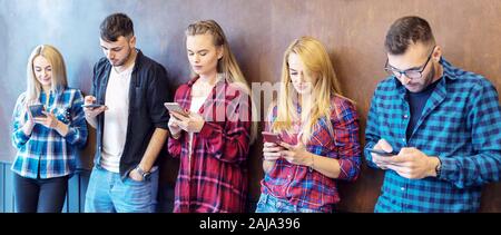 Happy young friends having fun using mobile phones against college wall Stock Photo