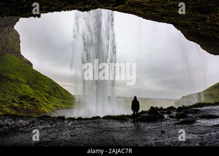 Female hiker looking at Seljalandsfoss waterfall inside a cave Stock Photo