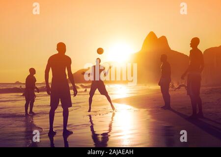 Silhouette of unidentified, unrecognizable locals playing ball game at sunset in Ipanema beach, Rio de Janeiro, Brazil. Stock Photo