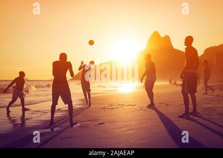Silhouette of unidentified, unrecognizable locals playing ball at sunset in Ipanema beach, Rio de Janeiro, Brazil. Stock Photo