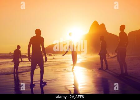 Silhouette of unidentified, unrecognizable locals playing ball game at sunset in Ipanema beach, Rio de Janeiro, Brazil. Stock Photo