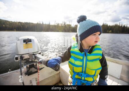 Young boy driving motor boat on calm lake on sunny day. Stock Photo