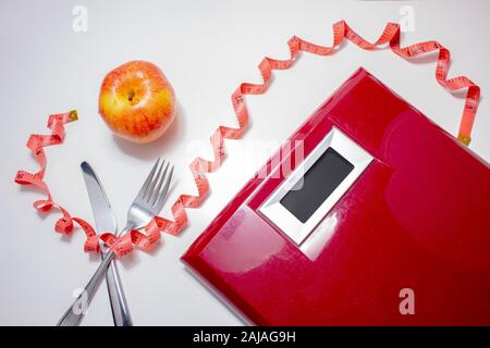 Losing weight concept. Weight scale with a fork, knife, red measuring tape and an apple Stock Photo