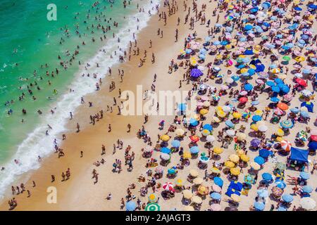 Rio de Janeiro, Brazil, aerial view of Copacabana Beach showing colourful umbrellas and people bathing in the ocean on a summer day.