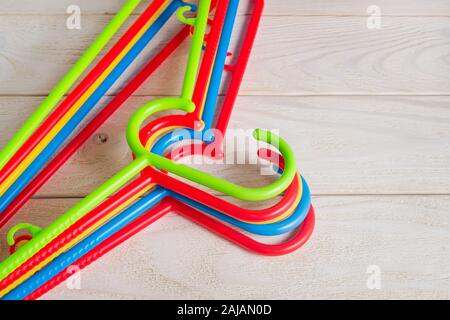 New multicolored plastic clothes hangers on a light wooden surface. Set of five colorful plastic clothes hangers. Household items. Domestic life. Stock Photo