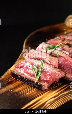 Juicy Beef Rib Eye Steak slices slightly salted, with herbs and spices on wooden board. Fresh grilled meat. Dark black background Stock Photo
