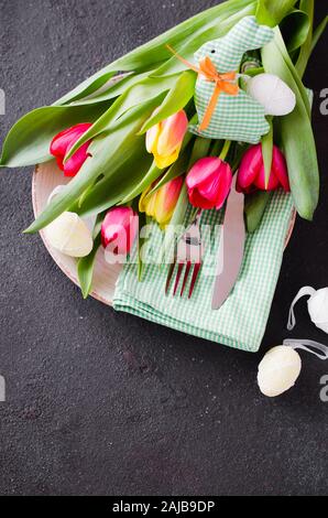 Easter table setting with bouquet of tulips and cutlery. Preparing for the festive Easter dinner. Top view. Stock Photo