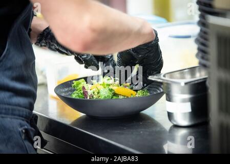 Closeup on hands of a cook preparing a salad in a kitchen with black plastic gloves Stock Photo