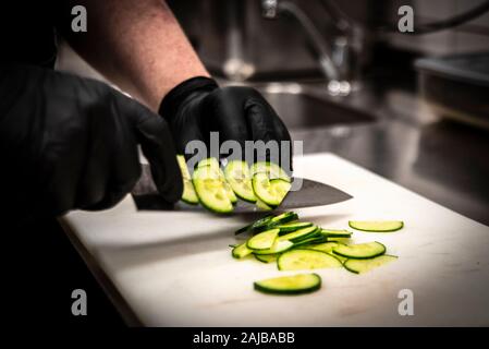 Closeup on hands of a cook preparing a salad in a kitchen with black plastic gloves Stock Photo
