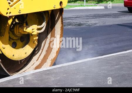 Road works ongoing, hot asphalt with steam and road roller on sunny day Stock Photo