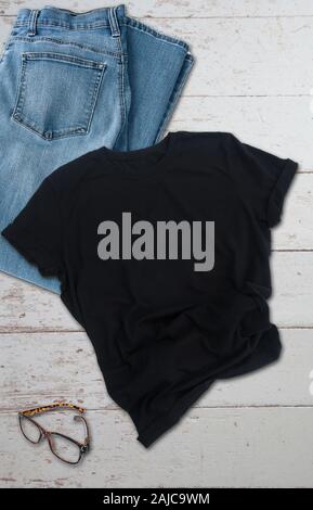 ck tshirt mockup with jeans styled product photo.  Blue jeans and a pair of glasses on distressed wood background with plenty of room for text or grap Stock Photo
