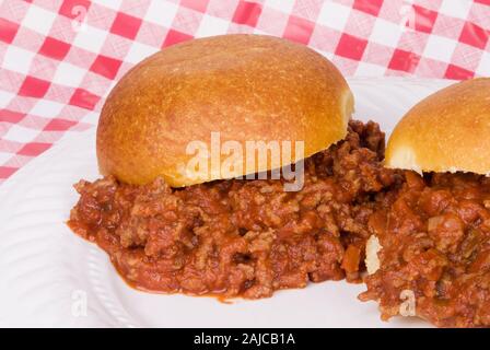 Homemade Sloppy Joe sandwiches served on a white plate with a red and white checkered tablecloth background. Stock Photo