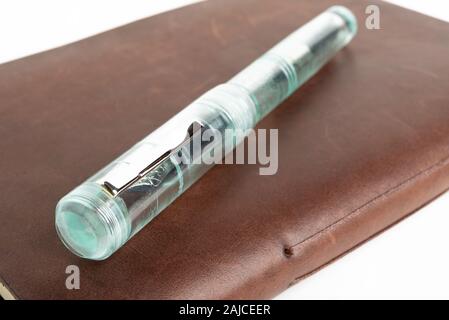 A simple but artful combination of classic leather-bound journal and green glass fountain pen set on a plain white background. Stock Photo
