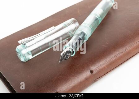 A simple but artful combination of classic leather-bound journal and green glass fountain pen set on a plain white background. Stock Photo