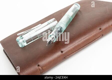 A simple but artful combination of classic leather-bound journal and green glass fountain pen set on a plain white background. Stock Photo