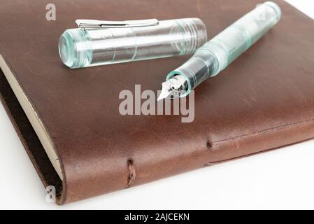 A simple but artful combination of classic leather-bound journal and green glass fountain pen set on a plain white background. Stock Photo