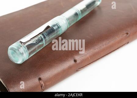 A simple but artful combination of classic leather-bound journal and green glass fountain pen set on a plain white background. Stock Photo