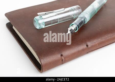 A simple but artful combination of classic leather-bound journal and green glass fountain pen set on a plain white background. Stock Photo