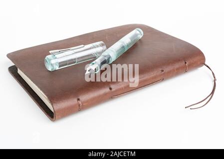 A simple but artful combination of classic leather-bound journal and green glass fountain pen set on a plain white background. Stock Photo