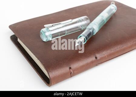 A simple but artful combination of classic leather-bound journal and green glass fountain pen set on a plain white background. Stock Photo