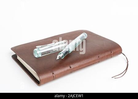 A simple but artful combination of classic leather-bound journal and green glass fountain pen set on a plain white background. Stock Photo