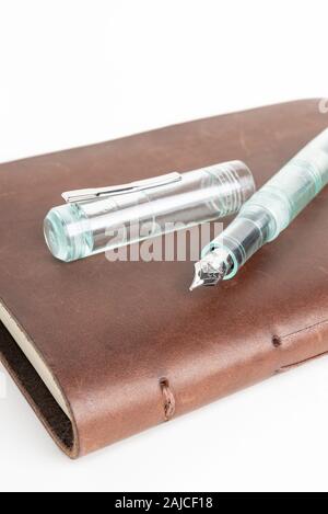 A simple but artful combination of classic leather-bound journal and green glass fountain pen set on a plain white background. Stock Photo