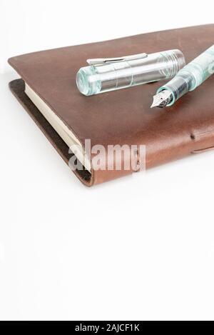 A simple but artful combination of classic leather-bound journal and green glass fountain pen set on a plain white background. Stock Photo