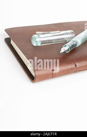 A simple but artful combination of classic leather-bound journal and green glass fountain pen set on a plain white background. Stock Photo