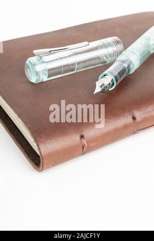 A simple but artful combination of classic leather-bound journal and green glass fountain pen set on a plain white background. Stock Photo