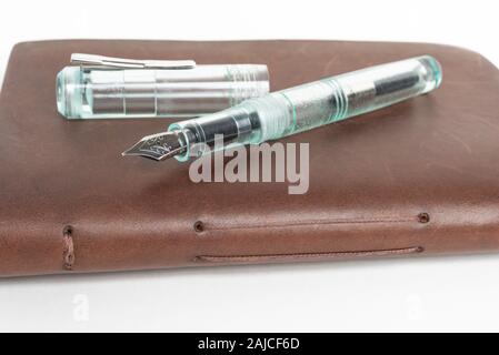 A simple but artful combination of classic leather-bound journal and green glass fountain pen set on a plain white background. Stock Photo