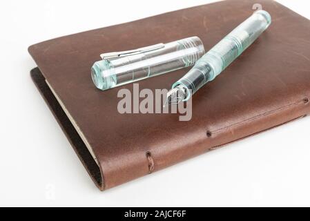 A simple but artful combination of classic leather-bound journal and green glass fountain pen set on a plain white background. Stock Photo