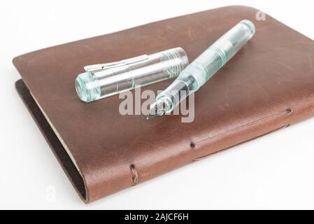 A simple but artful combination of classic leather-bound journal and green glass fountain pen set on a plain white background. Stock Photo